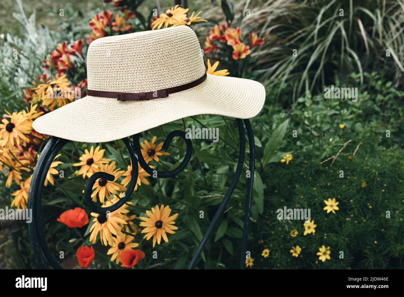 Women's summer hat on a green chair in a garden with flowers, nature ...