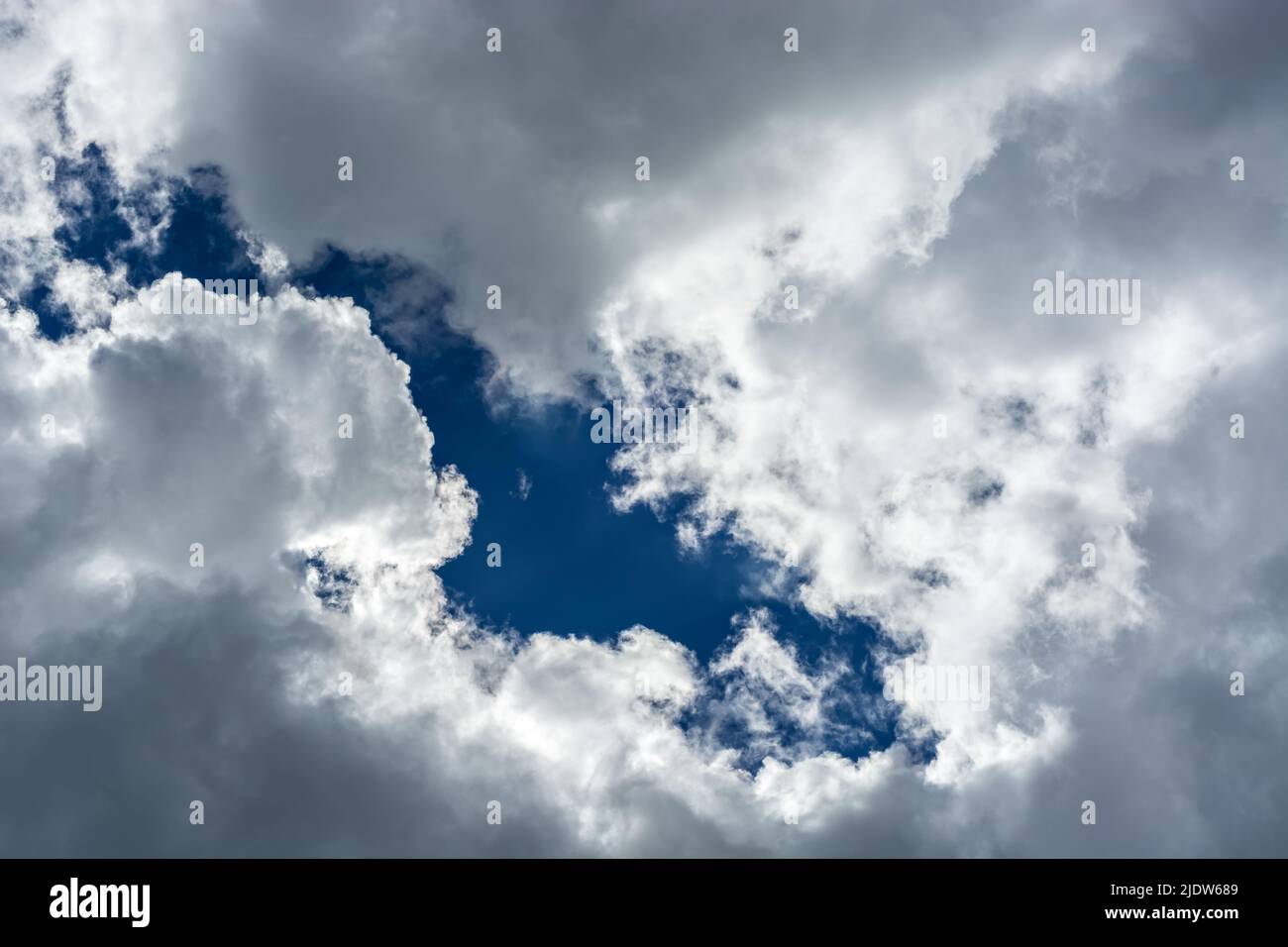 Fragment of a bright blue sky showing through gray fluffy clouds, for use as an abstract background and textures. Stock Photo