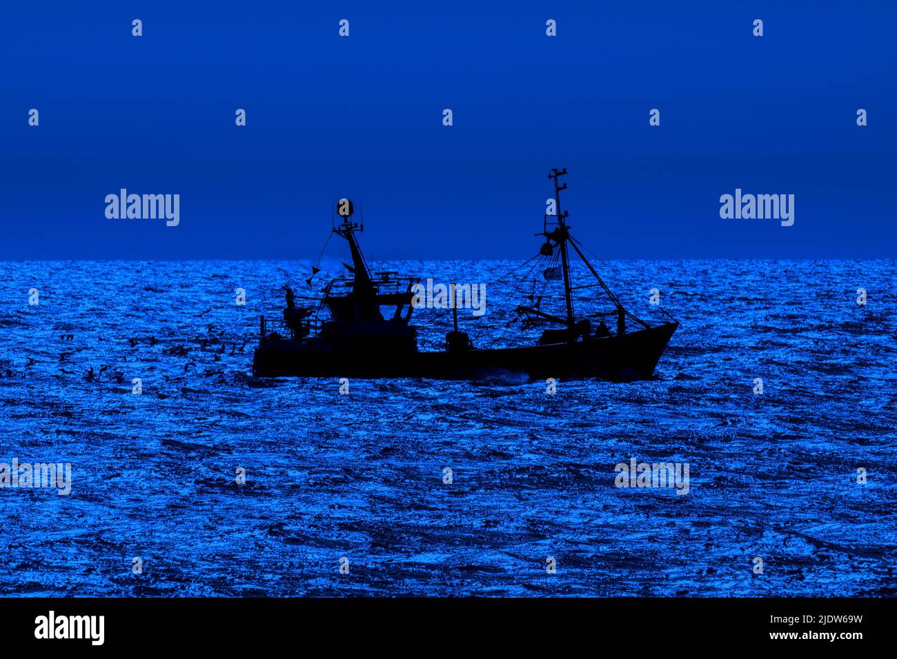 Bottom trawler, fishing boat sailing along the North Sea coast silhouetted against blue night sky in front of Nieuwpoort / Nieuport, Flanders, Belgium Stock Photo