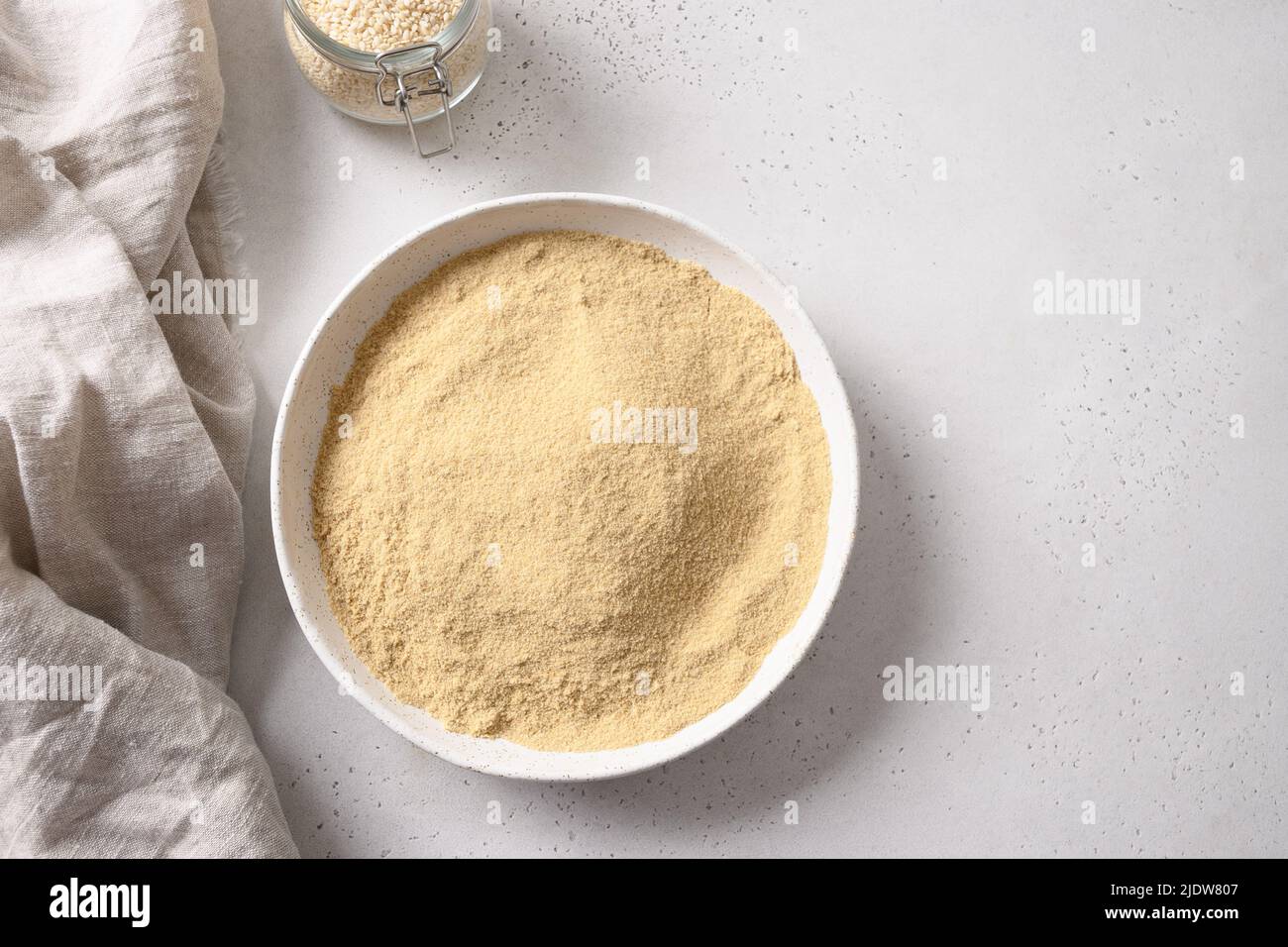 Sesame flour in white bowl and sesame seeds in spoon. Stock Photo