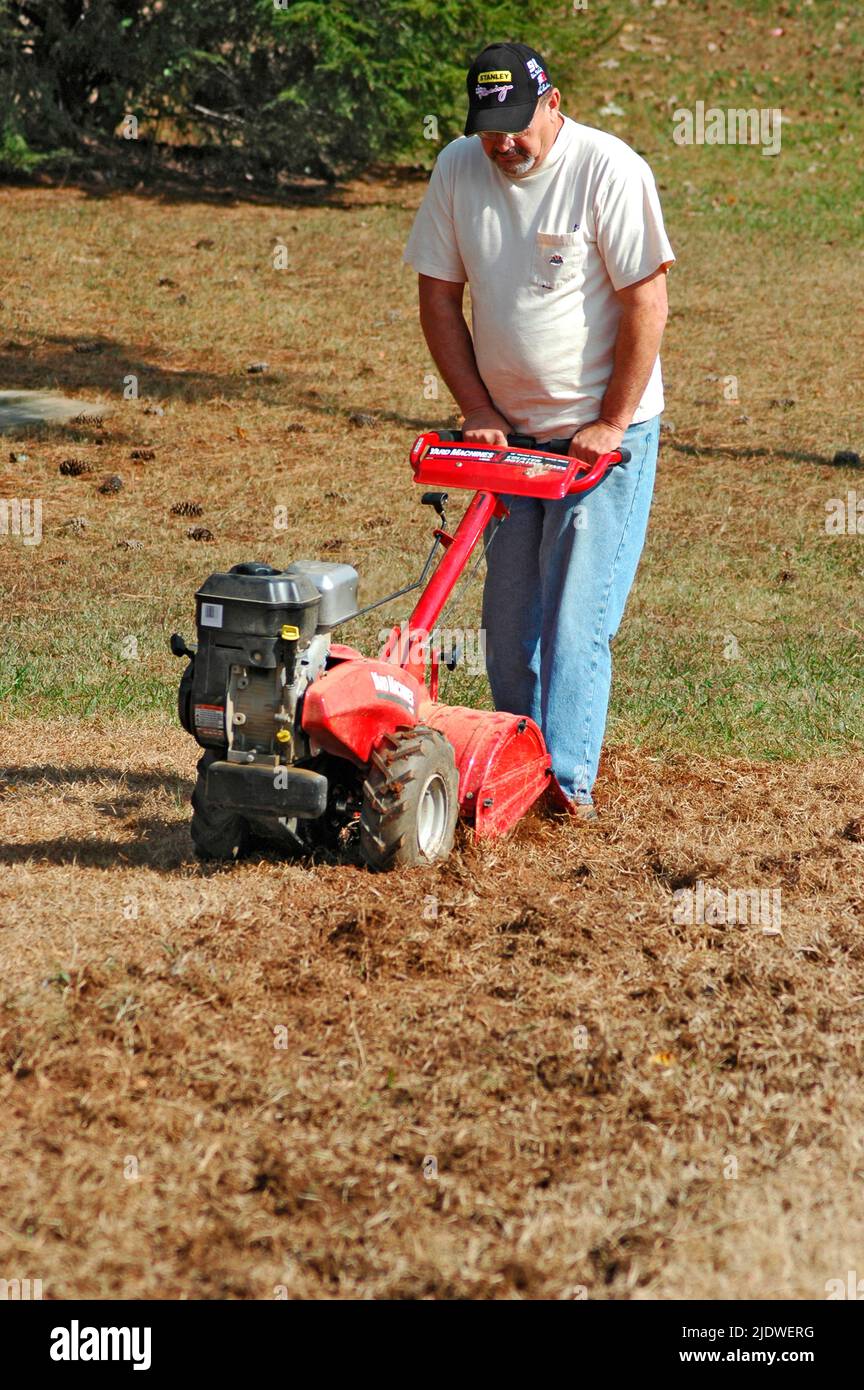 Men roto tilling a public lawn to put in garden with tillers, front and rear tines father and son, for the hungry and homeless Stock Photo