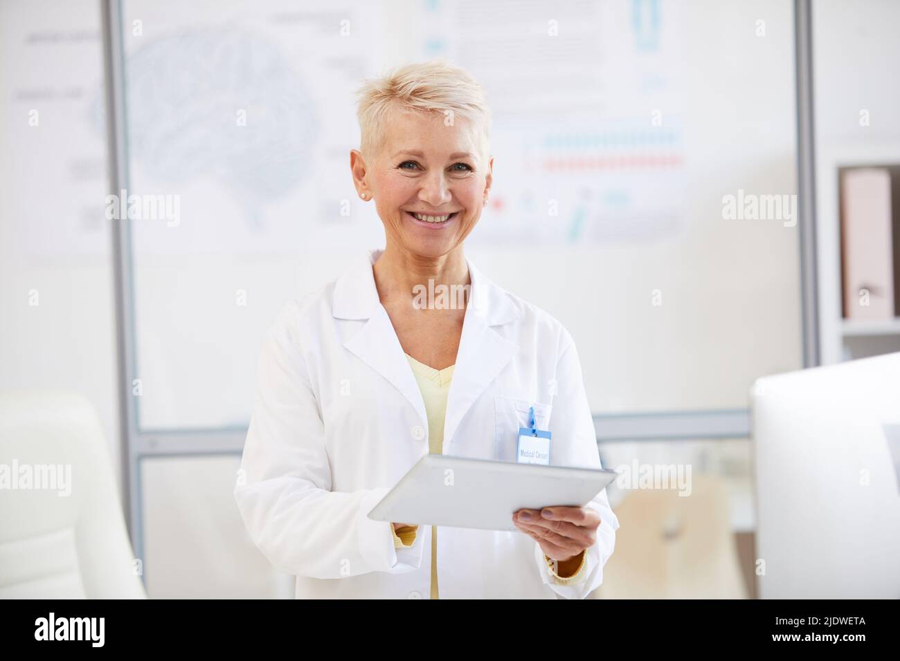 Portrait of cheerful beautiful female neurologist in lab coat using digital tablet at medical conference Stock Photo