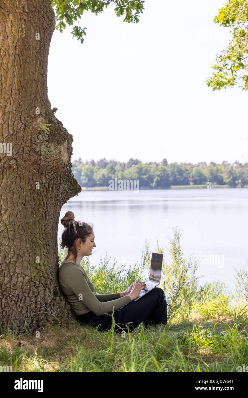 Work from anywhere. Remote freelancer work in nature. Young woman, female freelancer working with laptop with Beautiful view of forest and lake. freelancer paradise, freedom of teleworking. distance. High quality photo Stock Photo