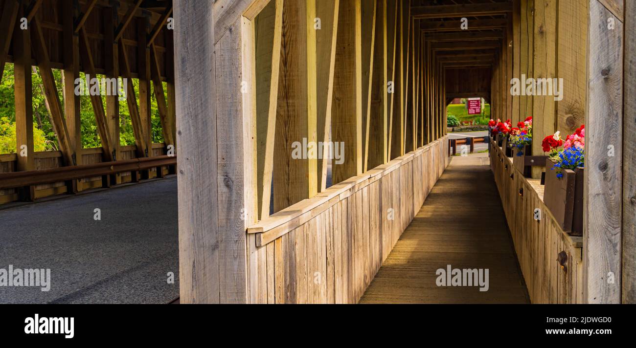 through a historic covered bridge along pedestrian walkway with flower boxes in bloom Stock Photo