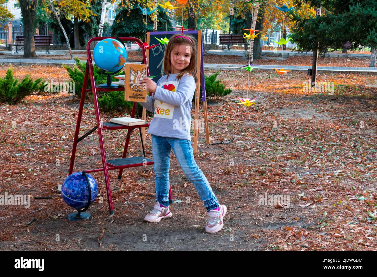 Lysychansk. Ukraine 10.04.2020 Adorable little schoolgirl against the background of an autumn park against the background of a school board and a Stock Photo