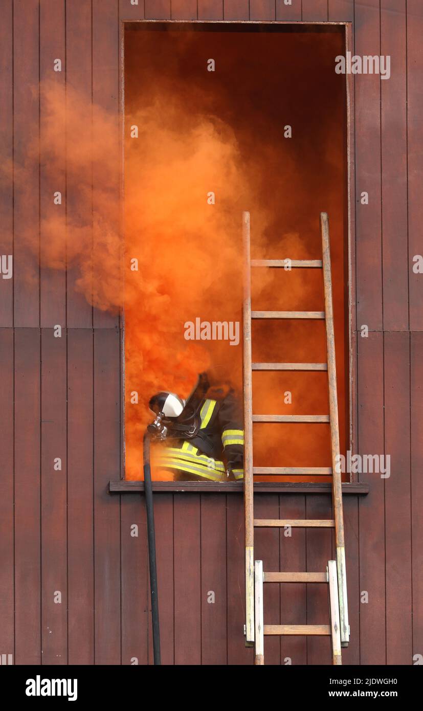 firefighters with a respirator and oxygen bottle nothing from a window completely vaulted with orange smoke and the ladders from which they climbed Stock Photo