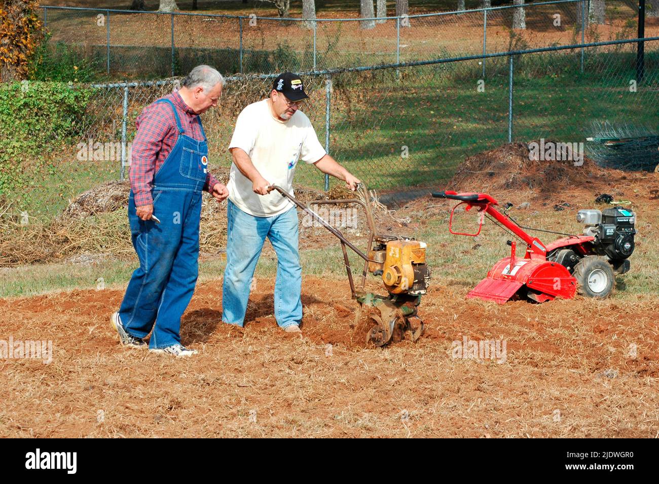 Men roto tilling a public lawn to put in garden with tillers, front and rear tines father and son, for the hungry and homeless Stock Photo