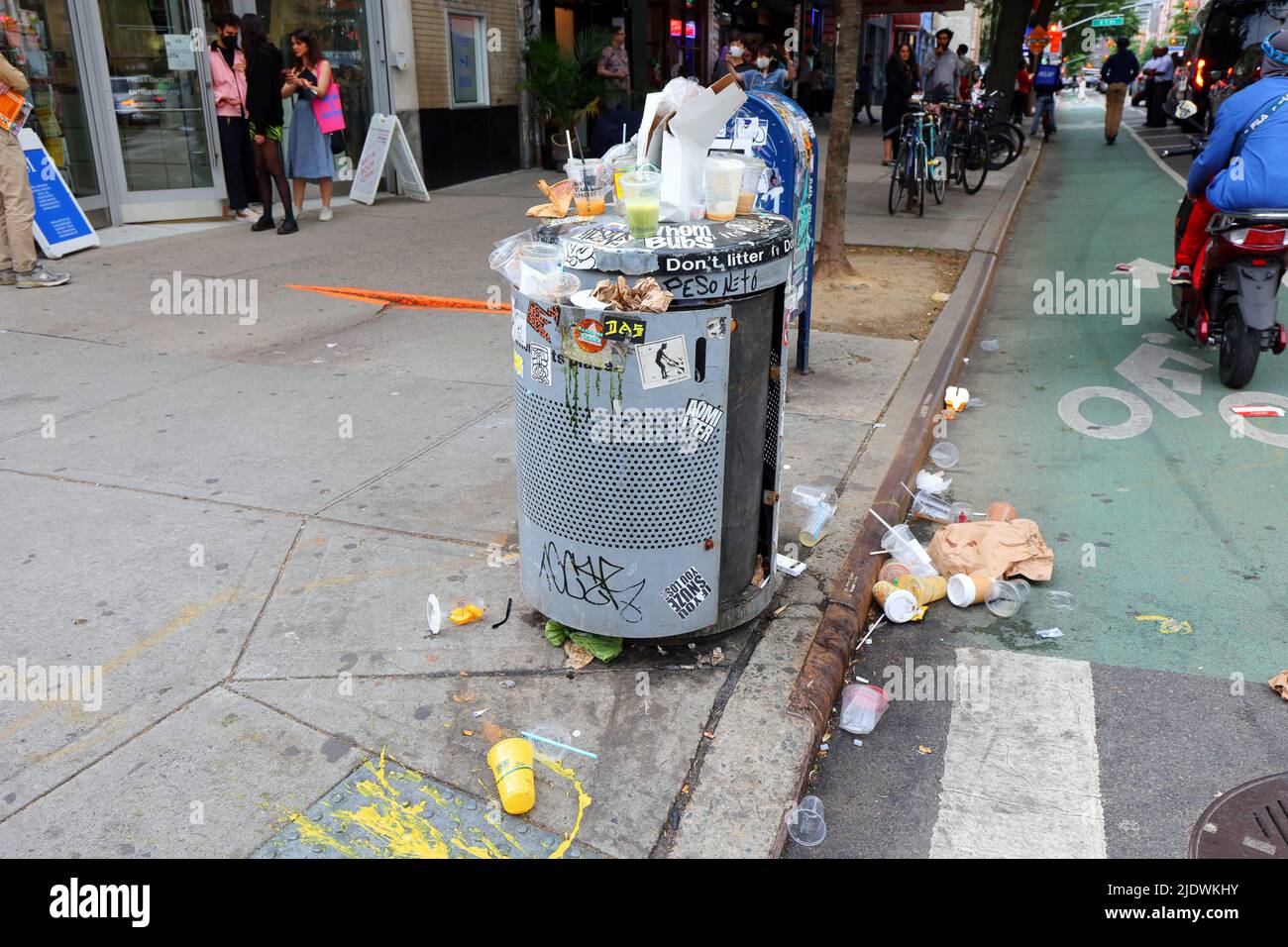 An overflowing trash can with litter on the sidewalk near a street corner on St. Marks Pl. in Manhattan's East Village neighborhood in New York City. Stock Photo