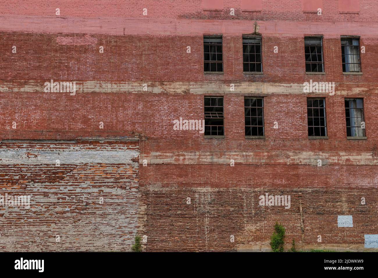An old warehouse exterior wall of crumbling brick and windows without glass. Stock Photo