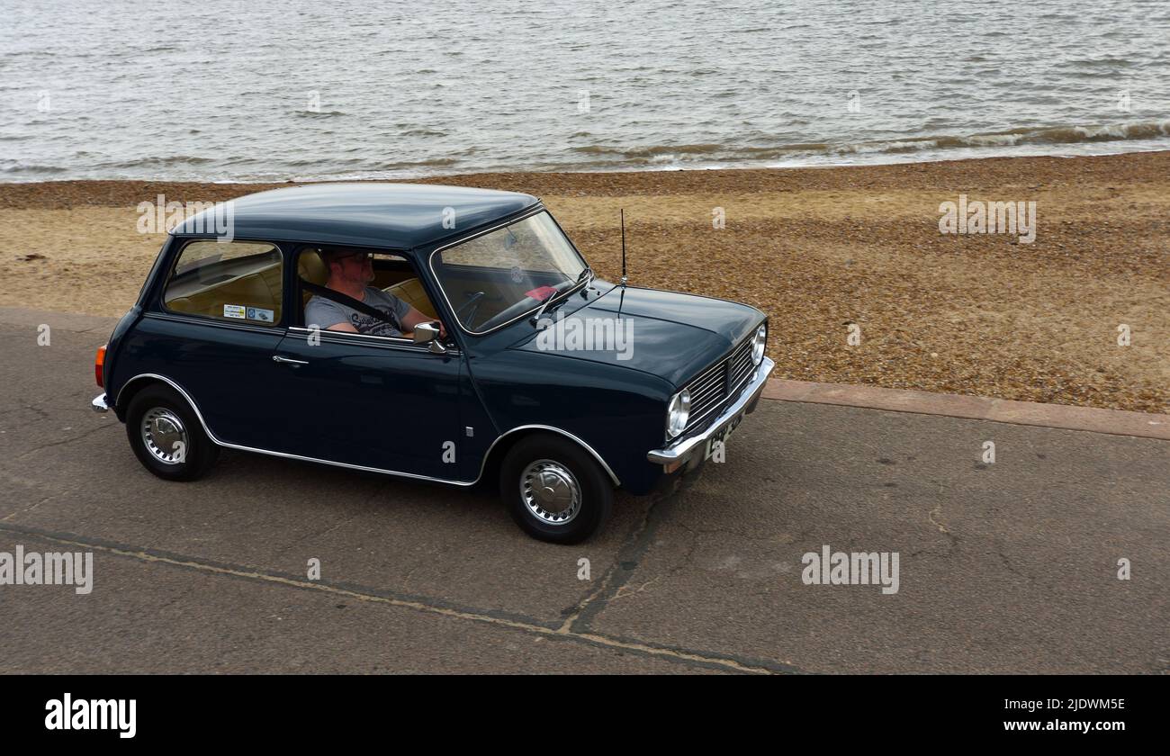 Classic Blue  Leyland Mini  being driven along seafront promenade ocean in background. Stock Photo