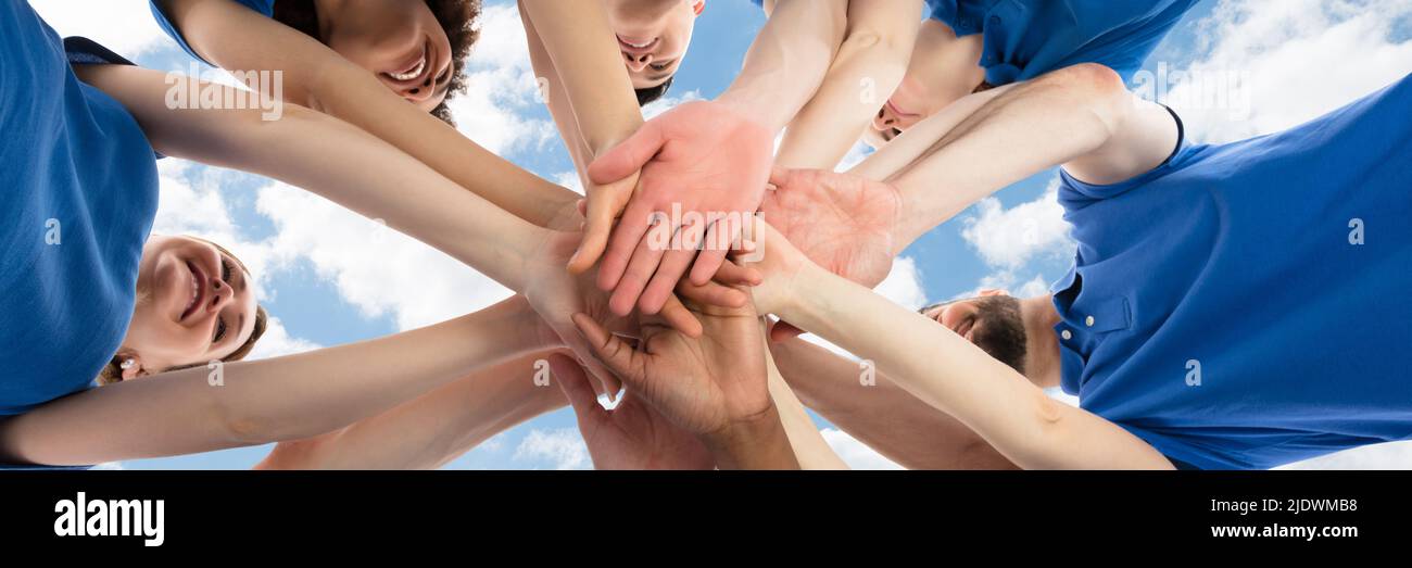Happy Multiracial Janitors Stacking Hands Against Cloudy Sky Stock Photo