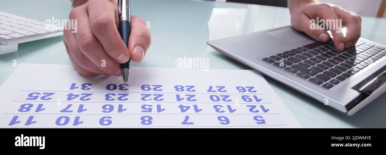 Close-up Of A Businessperson's Hand Marking With Pen On Calendar At Workplace Stock Photo