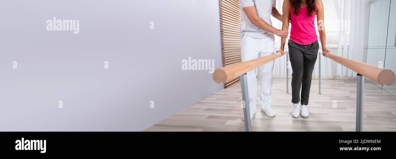 Female Patient Being Assisted By Physical Therapist While Walking With The Support Of Handrails Stock Photo