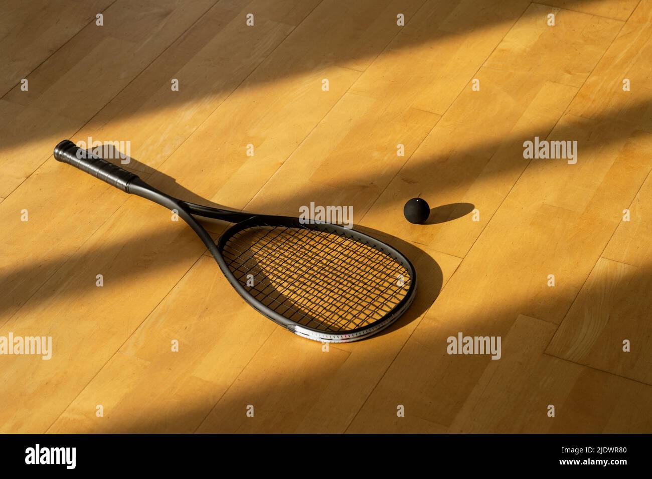 Black squash racket and ball with natural lighting on grey court. Horizontal sport theme poster, greeting cards, headers, website and app Stock Photo