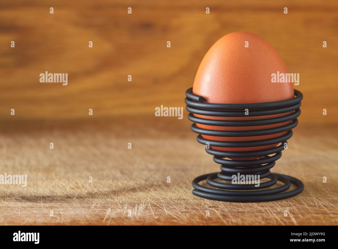 One boiled egg in a spiral-shaped metal support on wood background with copy space Stock Photo