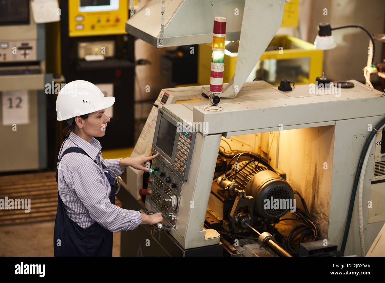 Serious busy female technical engineer standing at cnc lathe and pushing buttons while choosing Cnc machining operations at factory Stock Photo