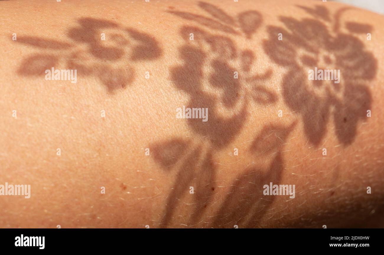 Shadow pattern of flowers on human skin. The play of light and shadow. Stock Photo