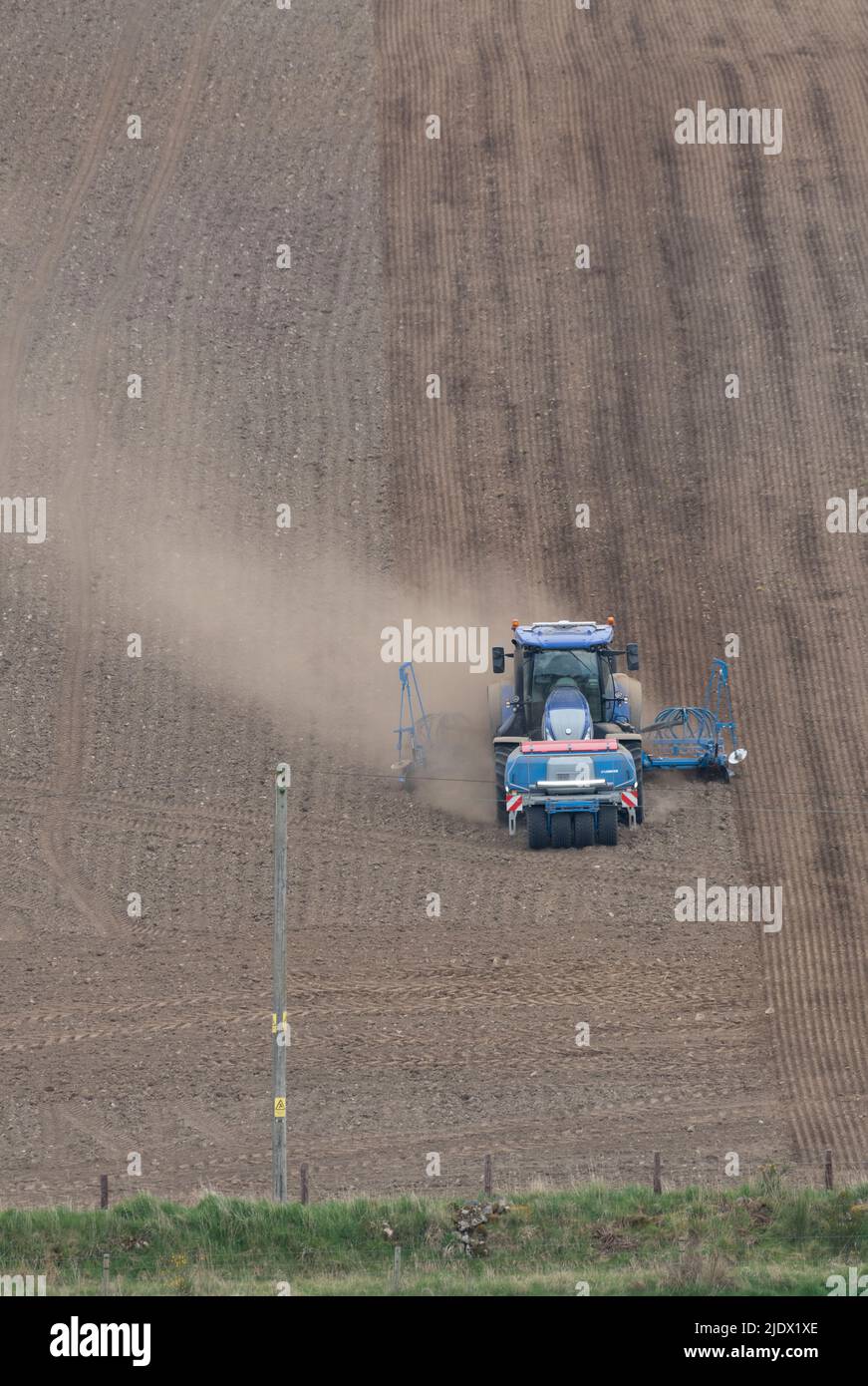 A Front View of a Blue Tractor with a Lemken Seed Drill Sowing Spring Barley as it Heads Down a Hillside Field in Clouds of Dust Stock Photo