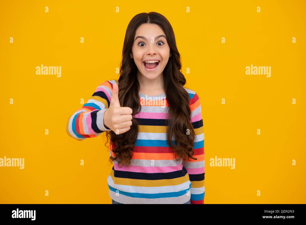 Amazed teenager. Excited teen girl. Happy casual teenager child girl showing thumb up and smiling isolated on yellow background. Stock Photo