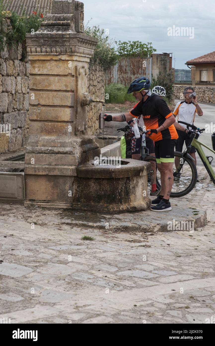 Spain, Castrojeriz, Castilla y Leon. Cyclists Filling Water Bottles at Town Fountain. Stock Photo
