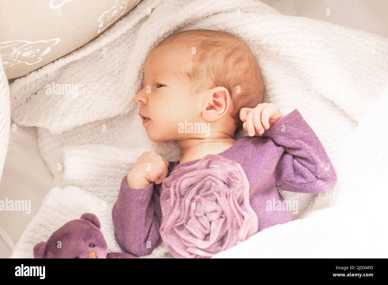 Cute newborn baby girl sleeps at home in her crib with her favorite toy