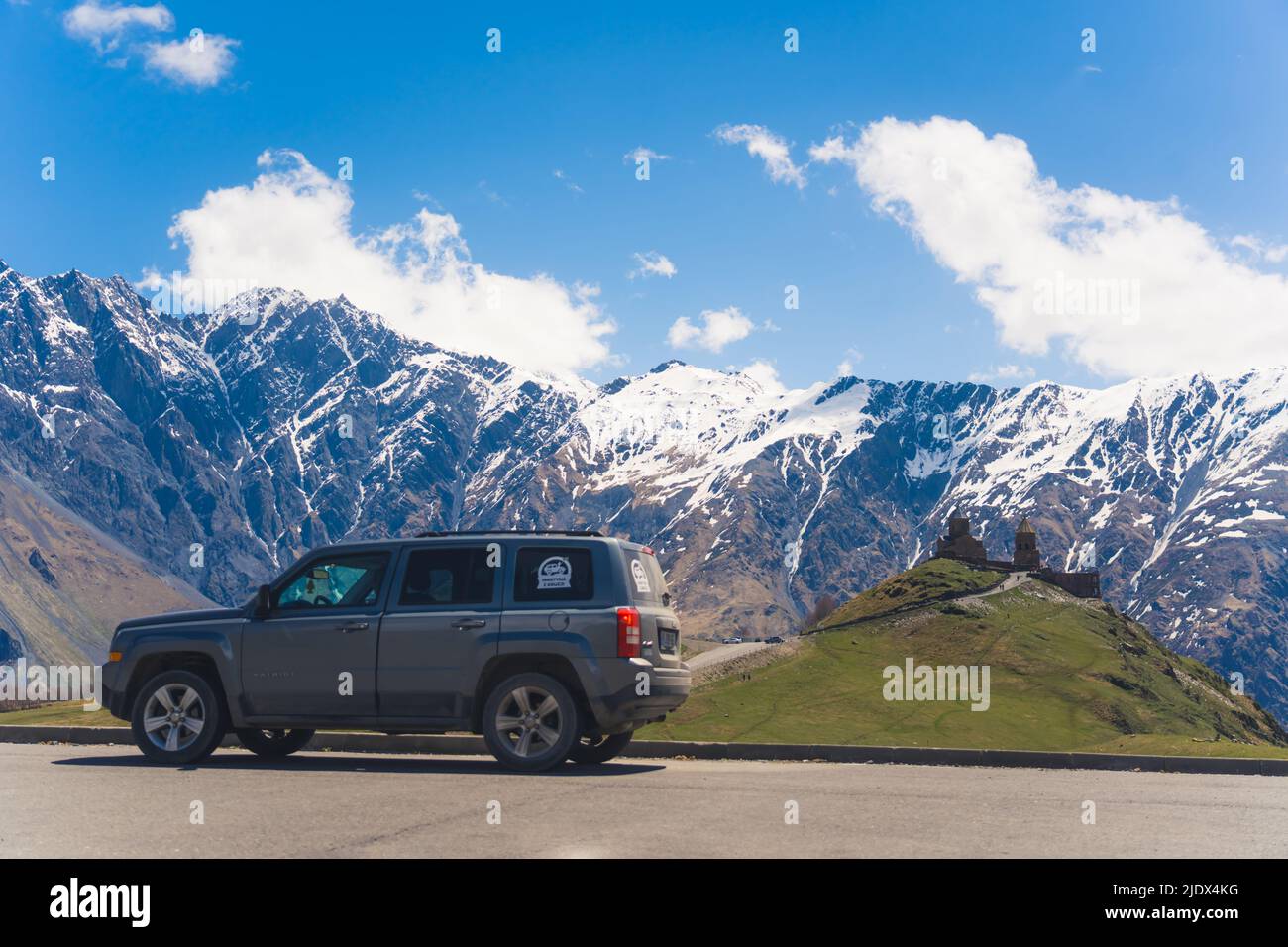 a car in the background of Gergeti Trinity Church and the incredible Caucasus mountains, Kazbegi, Georgia. High quality photo Stock Photo