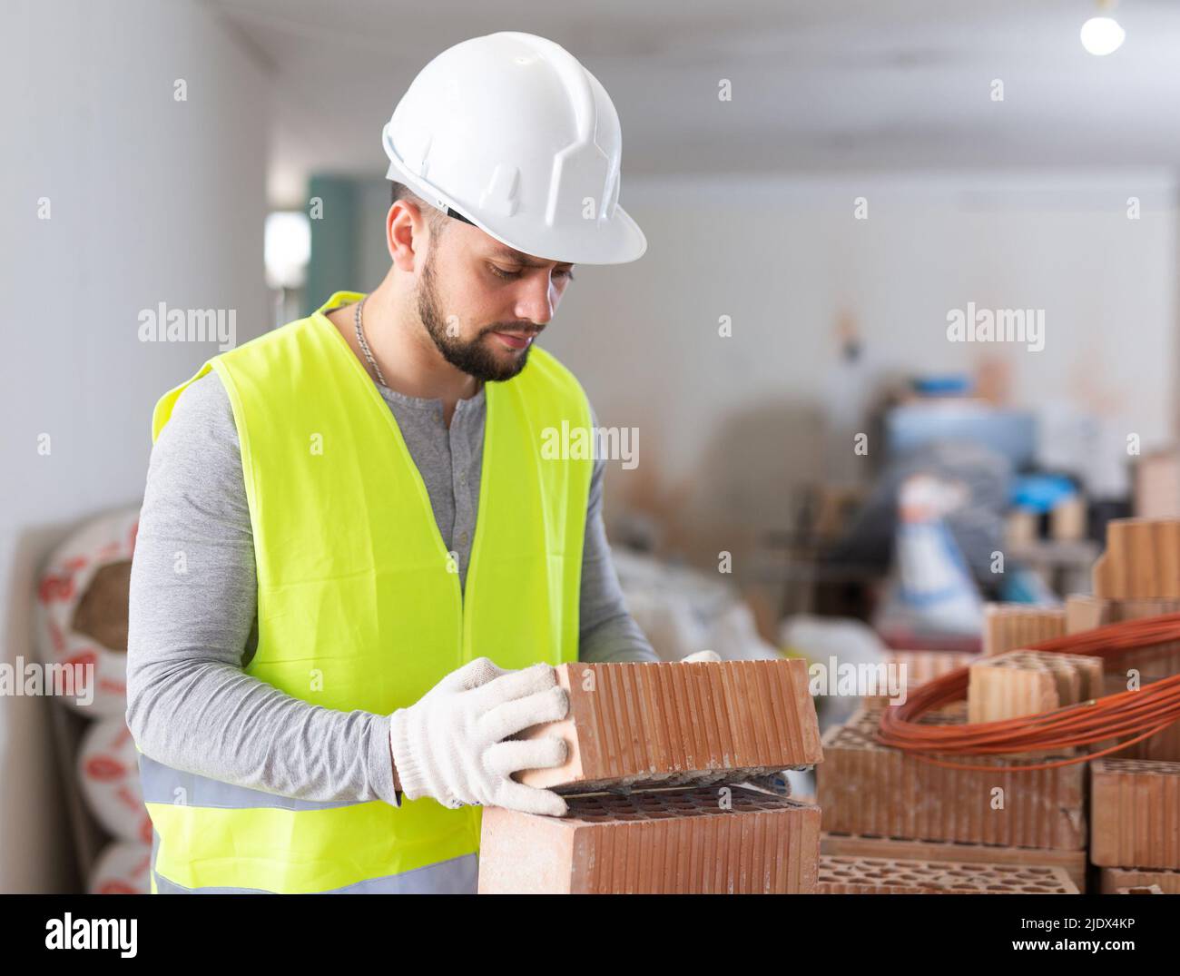 Young builder inspects and stacks bricks on top of each other Stock ...