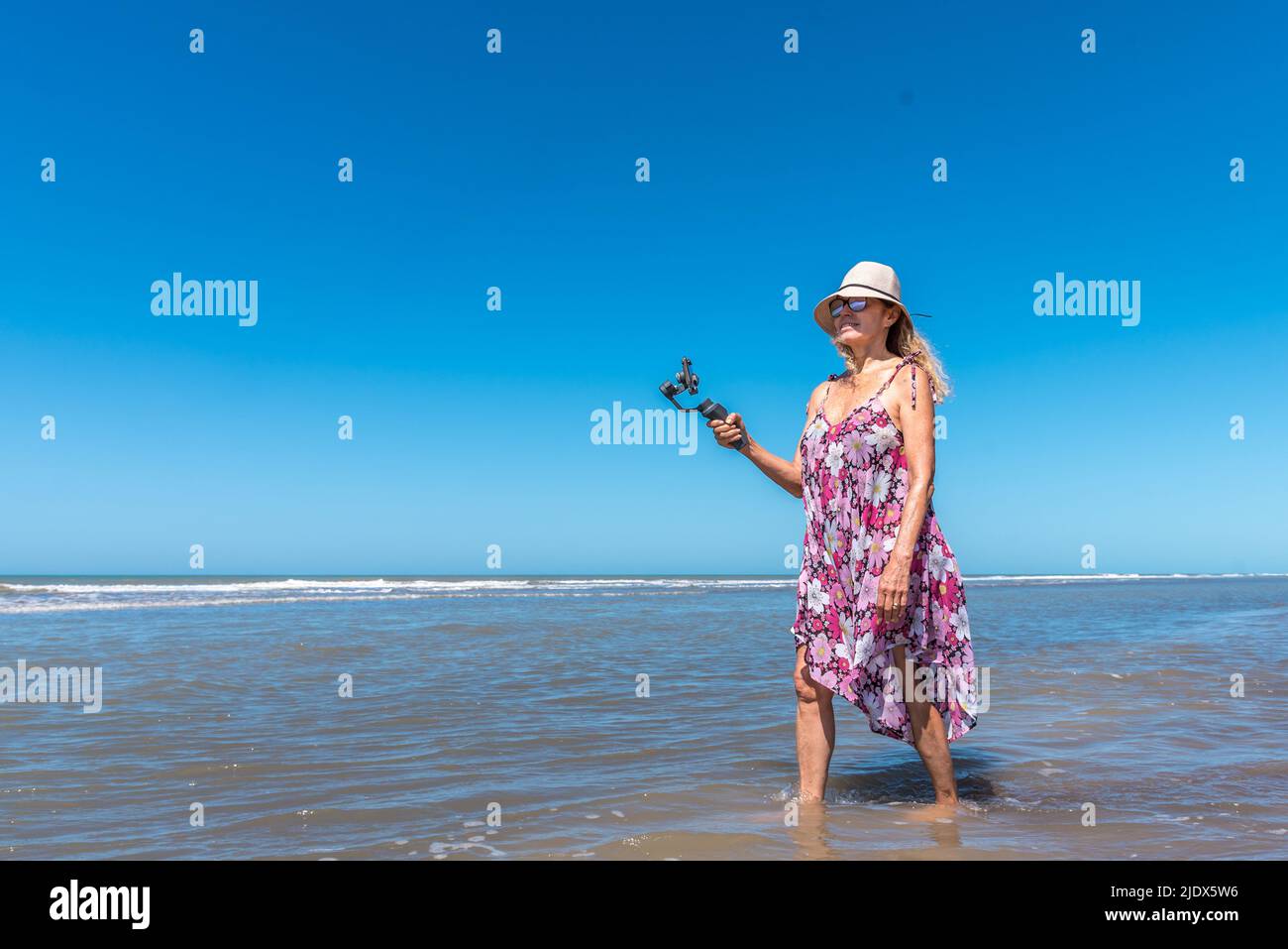 Panoramic photography of a woman walking into the water of the sea while filming with a mobile Stock Photo