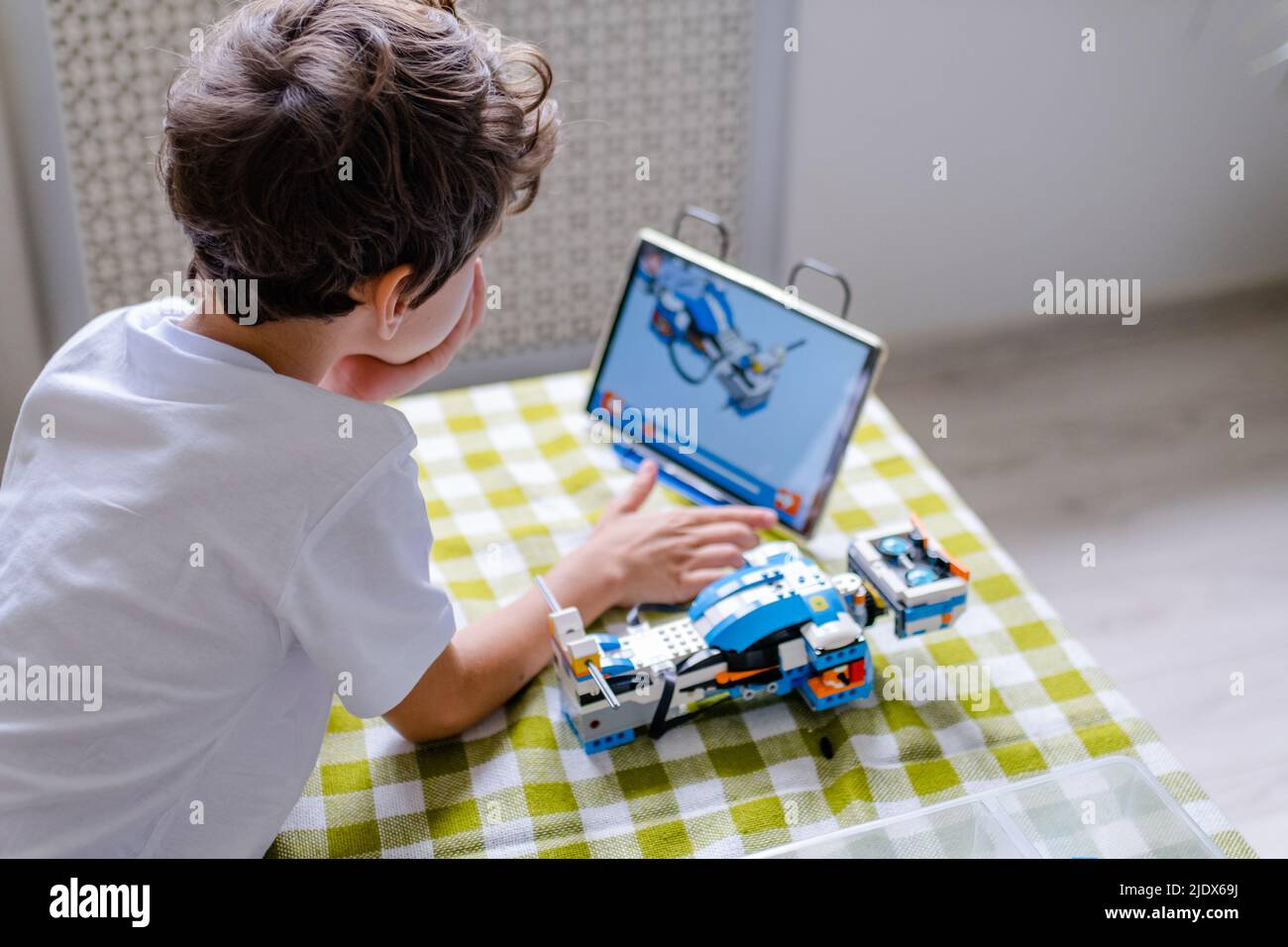 Kid collects robot from plastics details and programmed on tablet, robotics. Stock Photo