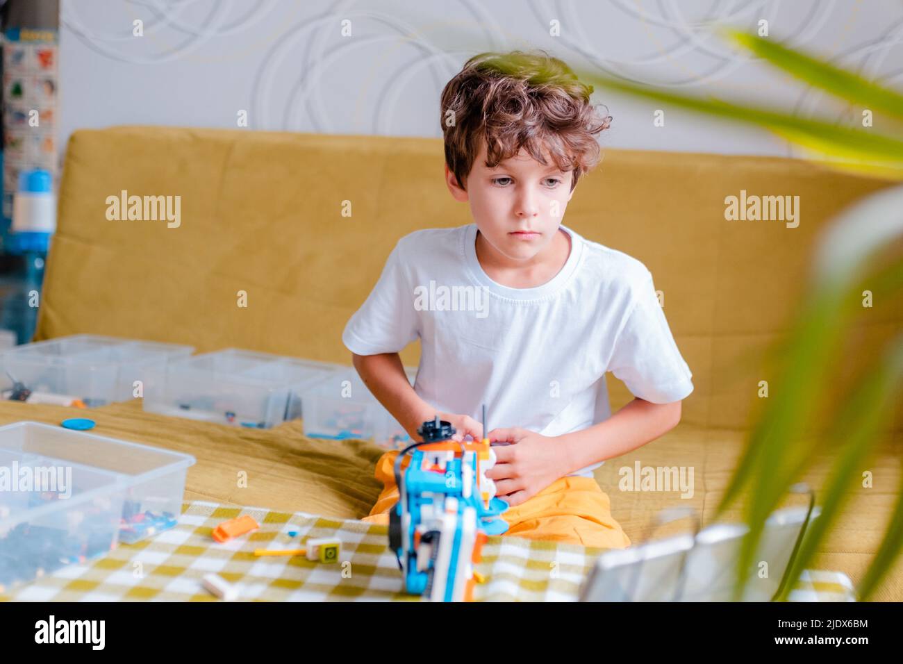 Kid collects robot from plastics details and programmed on tablet, robotics. Stock Photo