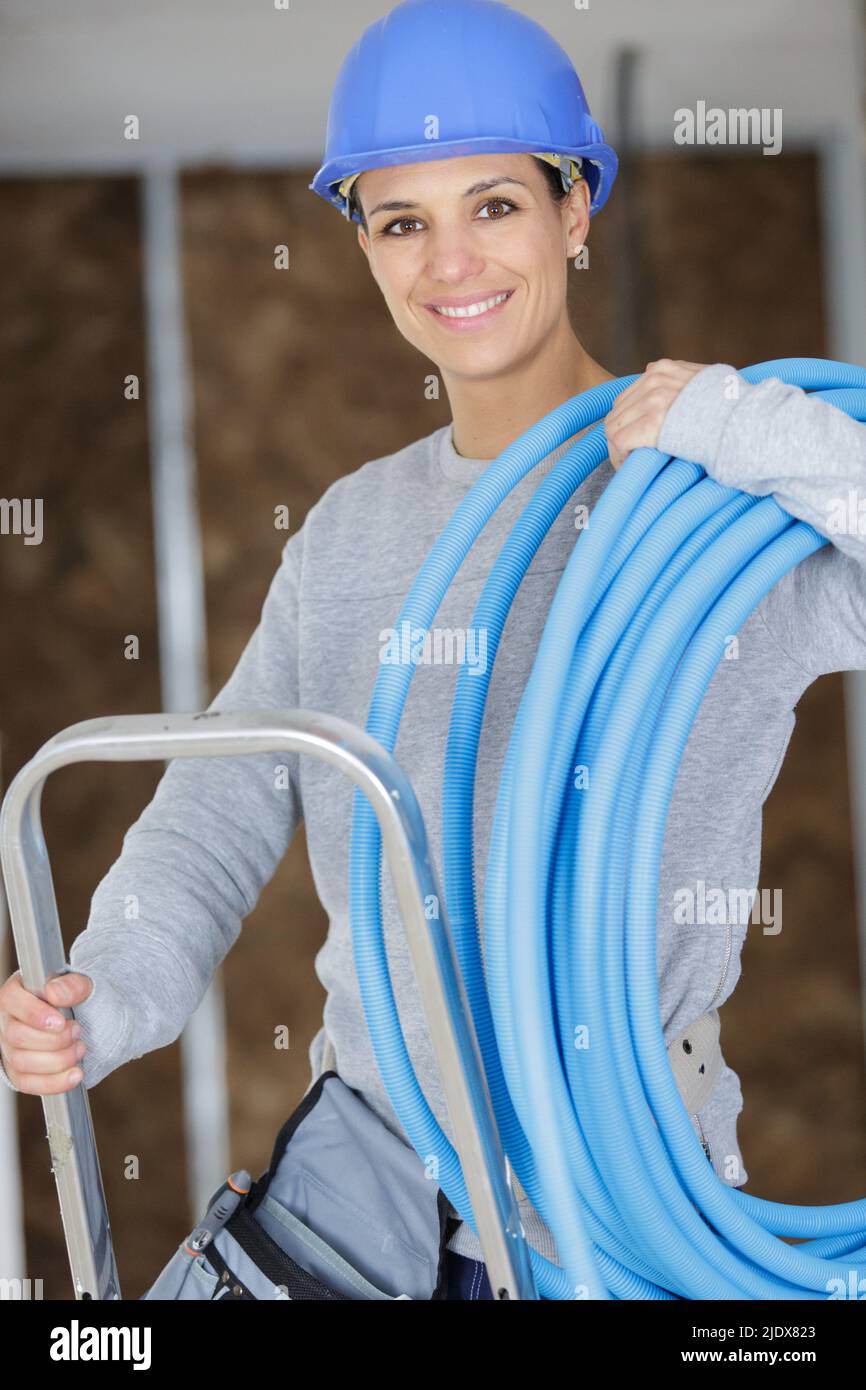 female builder on stepladder holding blue pipe Stock Photo