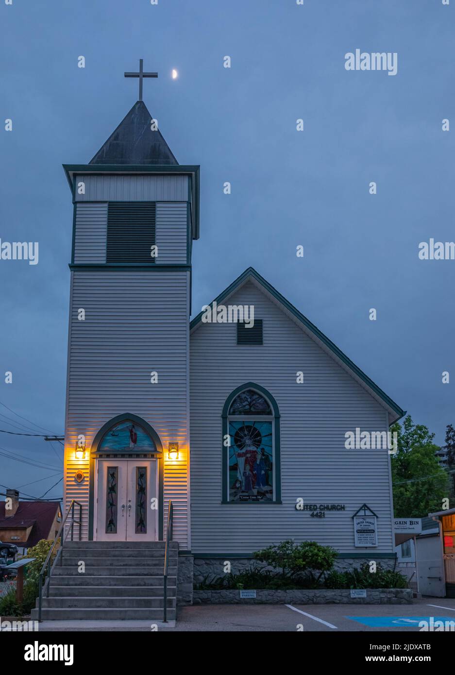 An old white christian church in rural Canada at nightfall. Wooden chapel with night lights. Stock Photo