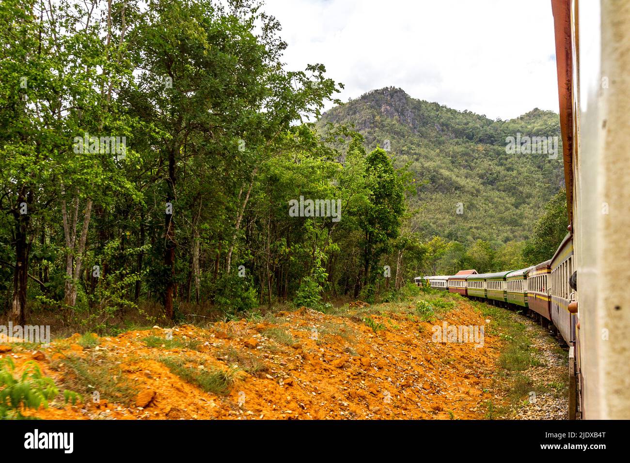 From the window of a moving train as the train rounds a curve in Thailand on the Dealh Railway looking back a the long row of train cars from behind. Stock Photo