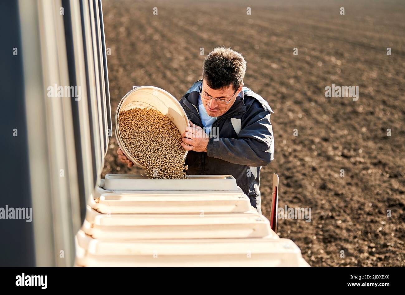Male farmer pouring soybean seeds in machine at field Stock Photo