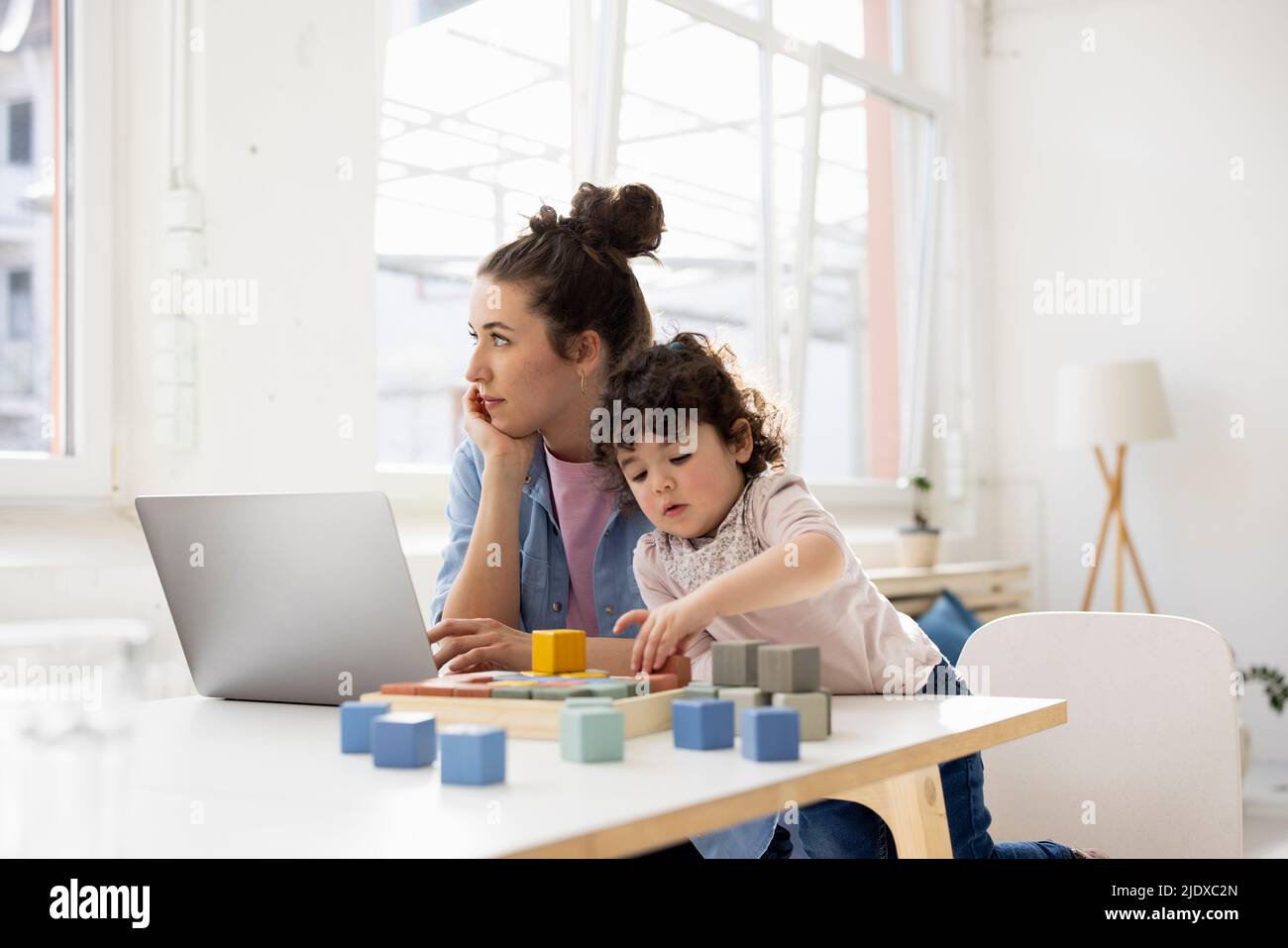Mother working from home using laptop while daughter is playing with buiilding blocks Stock