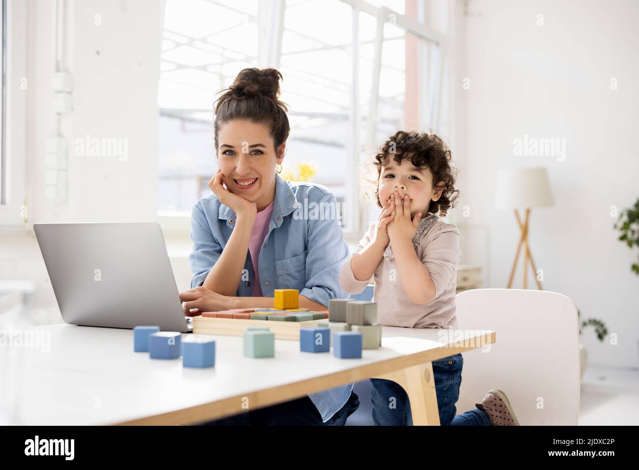 Mother working from home using laptop while daughter is playing with buiilding blocks Stock Photo