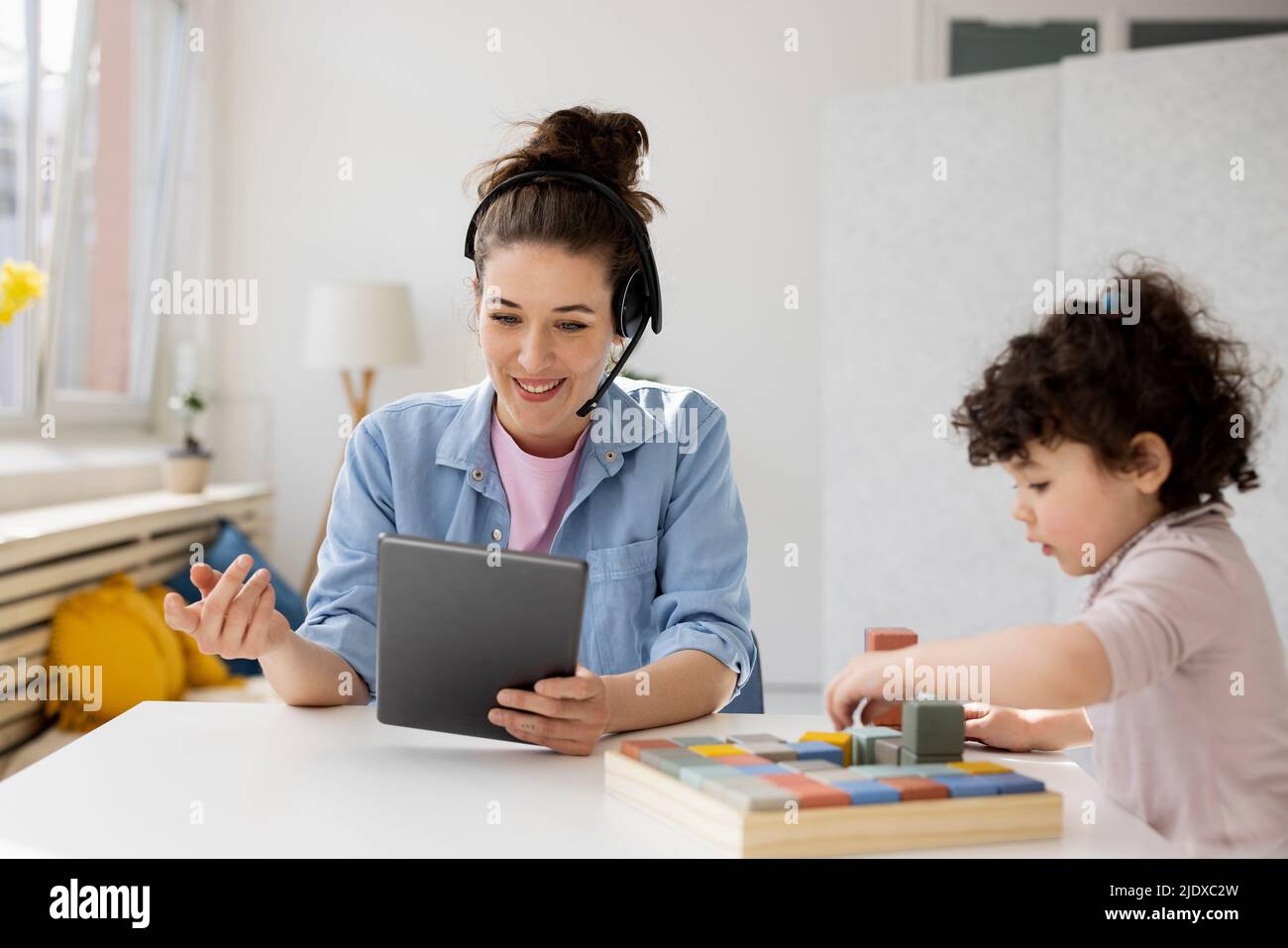 Mother working from home using digital tablet while daughter is playing with buiilding blocks Stock Photo