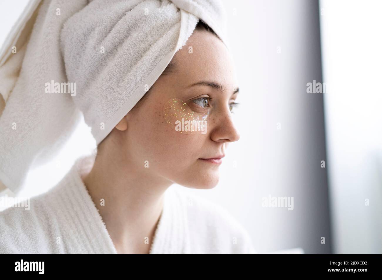 Thoughtful young woman with collagen eye mask wearing towel at home Stock Photo