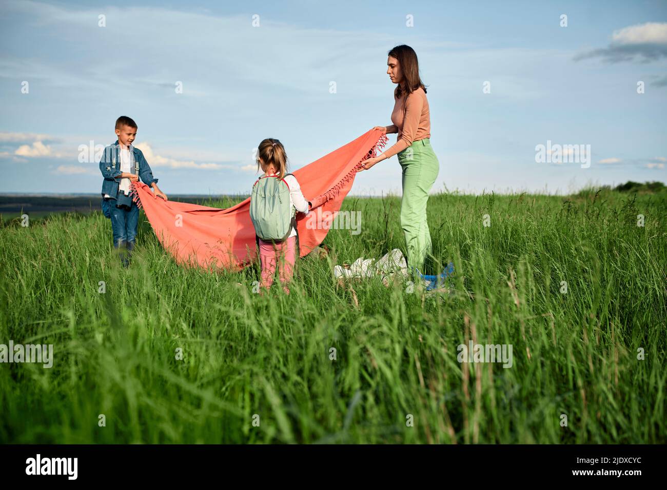 Mother and children laying out picnic blanket on grass in field Stock