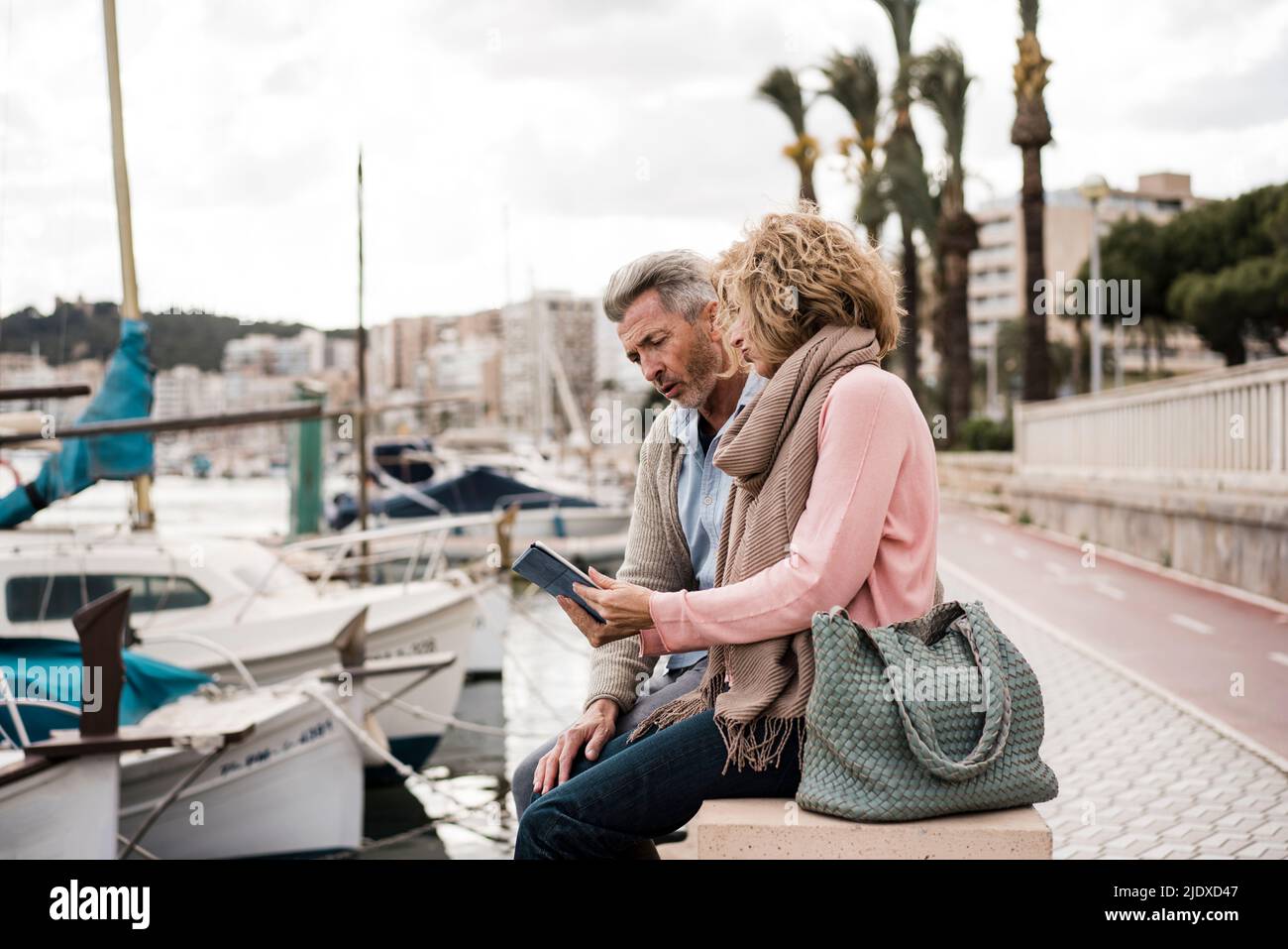 Mature couple reading book sitting at harbor on vacation Stock Photo