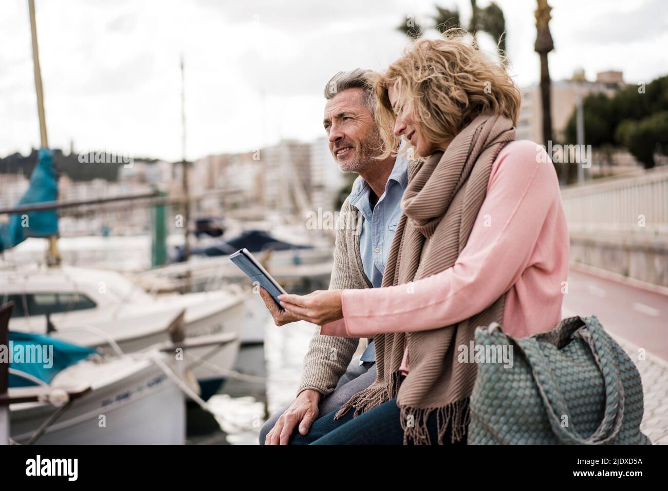 Mature woman reading book by man at harbor Stock Photo