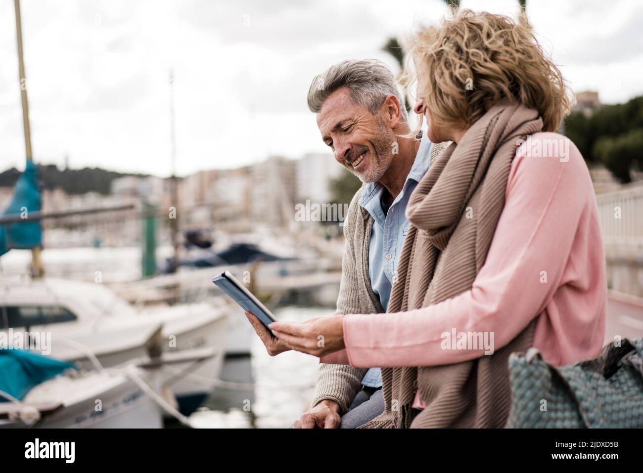 Smiling couple reading book sitting at harbor on vacation Stock Photo
