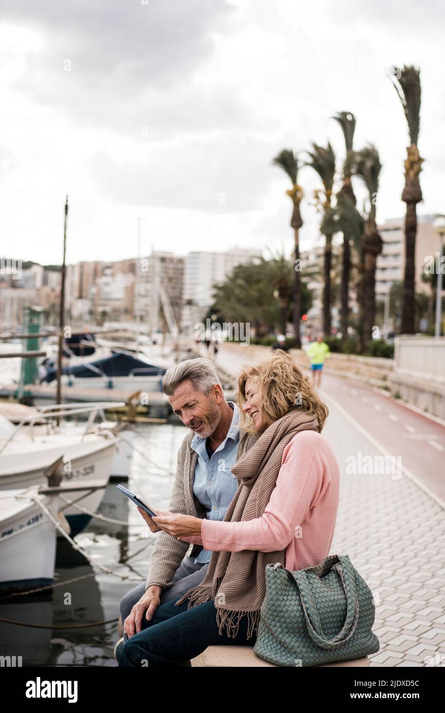 Mature couple reading book sitting at harbor in city Stock Photo