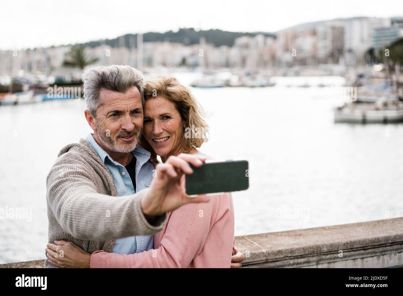 Smiling woman embracing man taking selfie in front of sea Stock Photo
