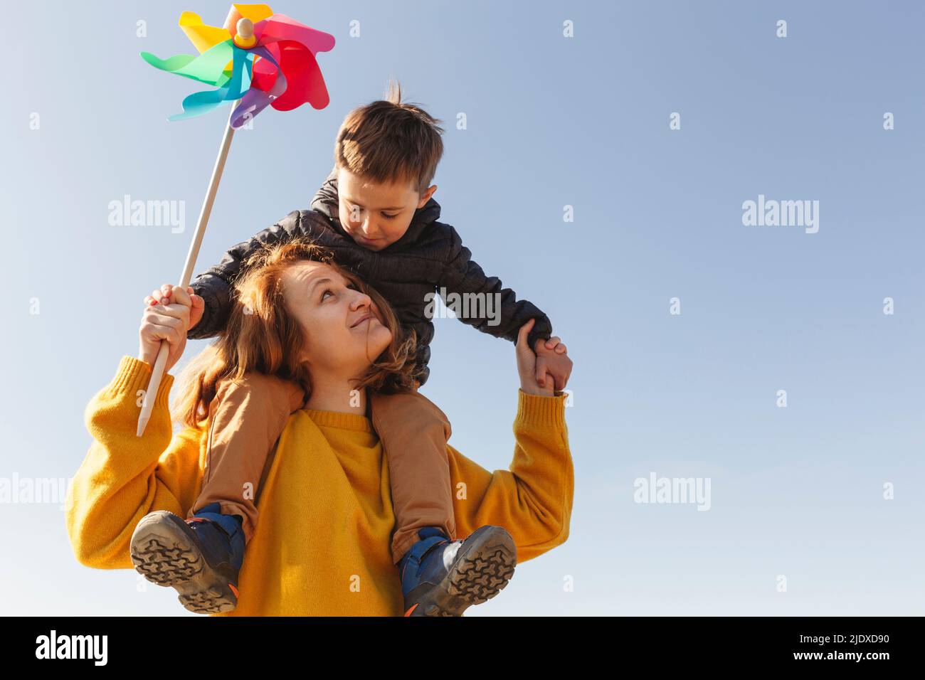 Happy woman carrying son on shoulders in front of blue sky Stock Photo