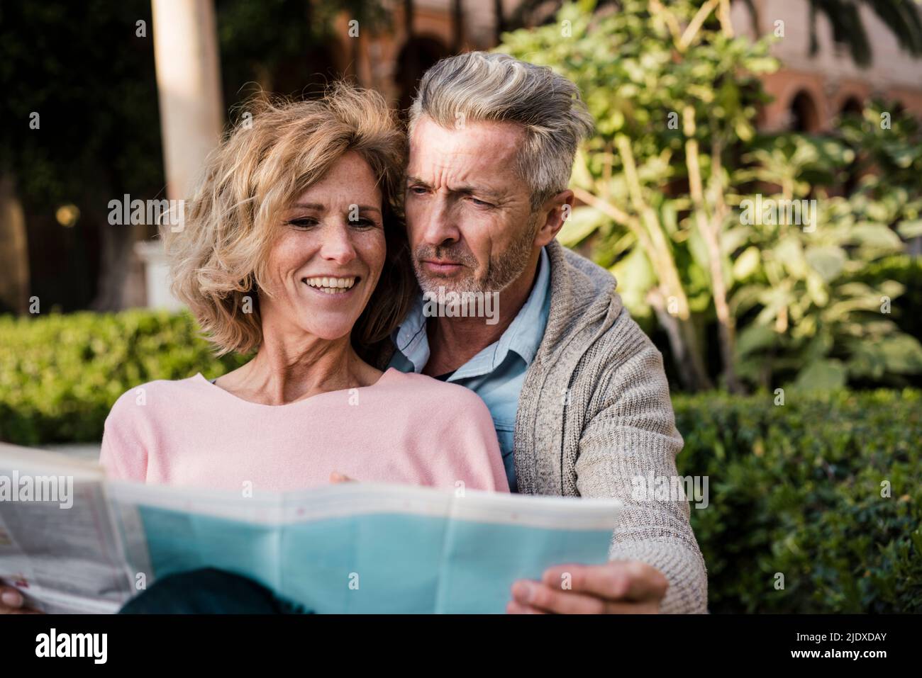 Smiling woman reading newspaper with man in park Stock Photo