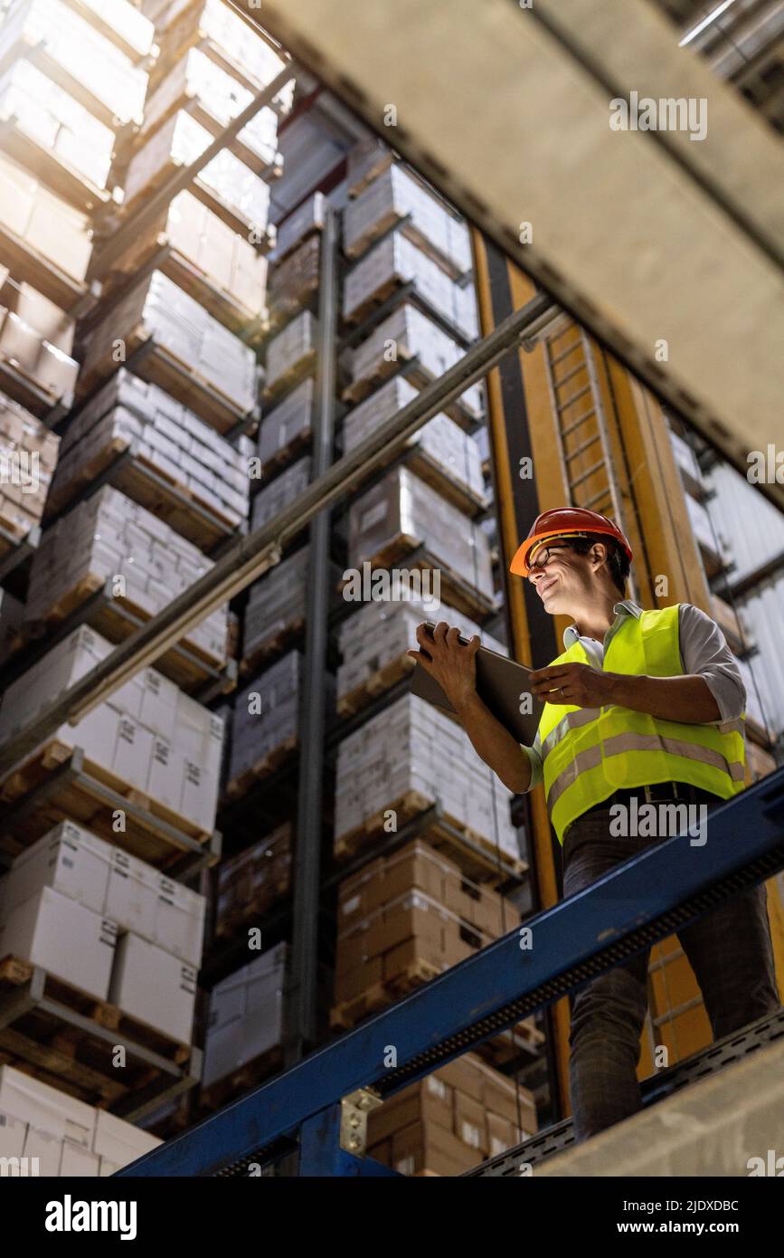 Smiling worker with tablet PC standing by railing in warehouse Stock Photo