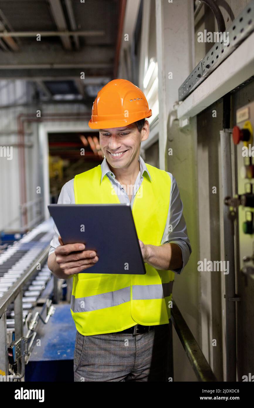 Smiling worker wearing hardhat using tablet PC in warehouse Stock Photo