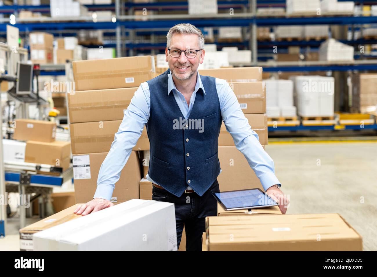 Smiling manager wearing eyeglasses leaning on cardboard boxes in warehouse Stock Photo Alamy