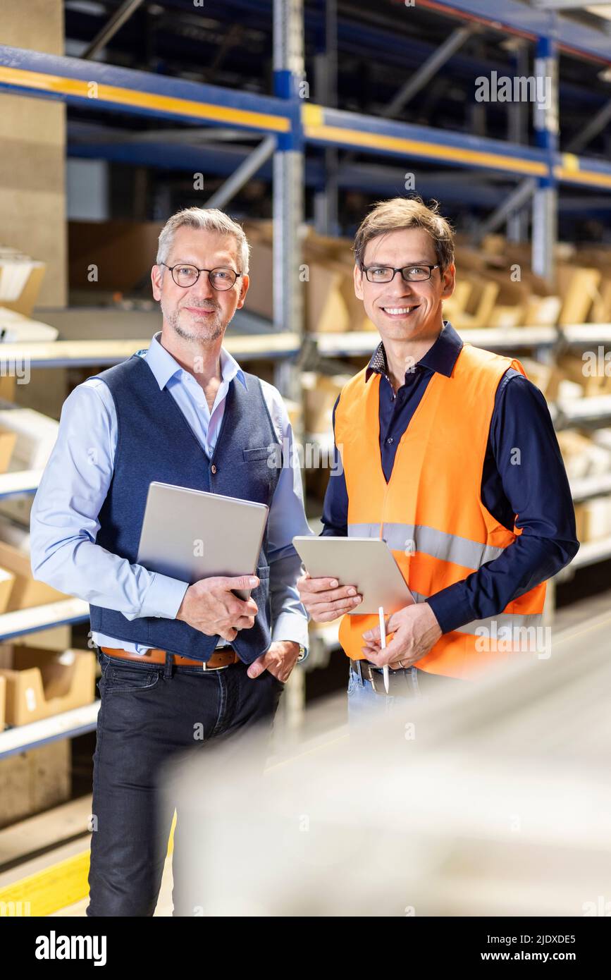 Smiling manager and worker with tablet PC standing in warehouse Stock Photo
